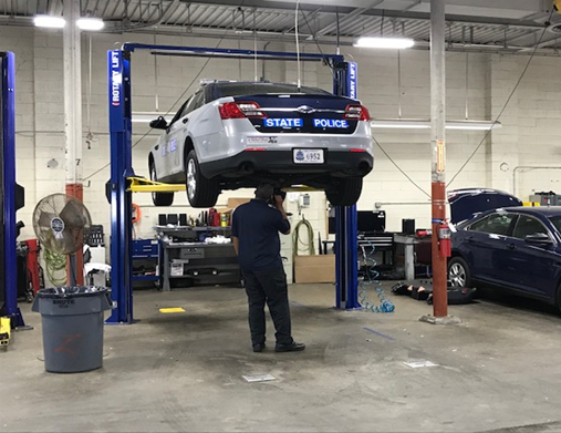 An employee checks a state police car raised on a lift.